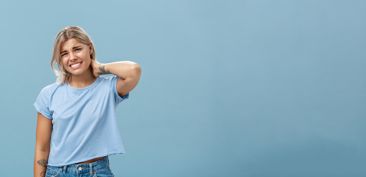 Girl Unwilling To Go With Friend Feeling Awkward And Unsure How Say No Frowning And Clenching Teeth Making Apologizing Face Rubbing Neck Behind Saying Sorry While Rejecting Offer Over Blue Background