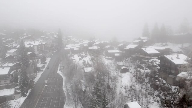Swiss mountain village Blatten Belalp with stables and chalets in fog and snow. Snowy landscape with snowy cottages in Swiss Alps.