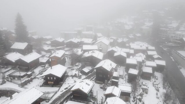 Snowy mountain village in the fog with small chalets, cottages and alpine huts. Aerial Shot
