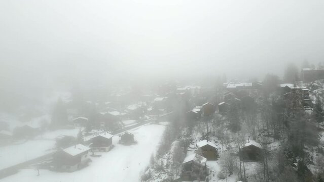 Aerial shot of a Swiss mountain village Blatten Belalp with cattle sheds and cottages in fog and snow. Swiss Alps snowy landscape with chalets covered with snow.