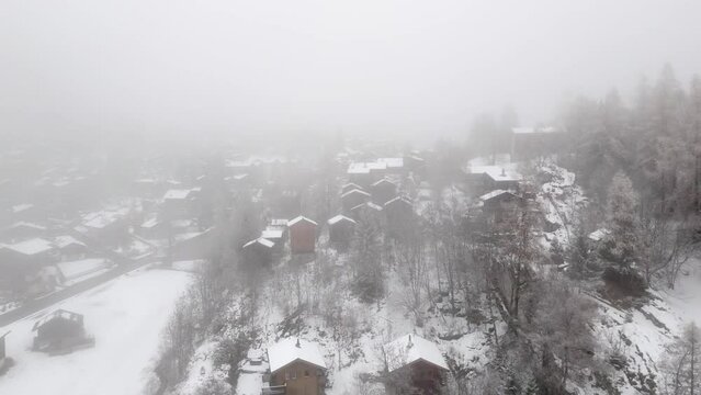 Aerial view of a Swiss mountain village Blatten Belalp with stables and huts in fog and snow. Snowy landscape with snowy cottages in Swiss Alps