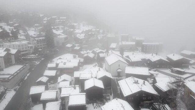 Small Swiss village Blatten near Belalp in the mountains with fog and snow. Small chalets, cottages and alpine huts. Aerial Shot