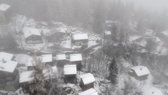 Snowy winter landscape with small chalets, cottages and alpine huts. A village in the mountains in the fog