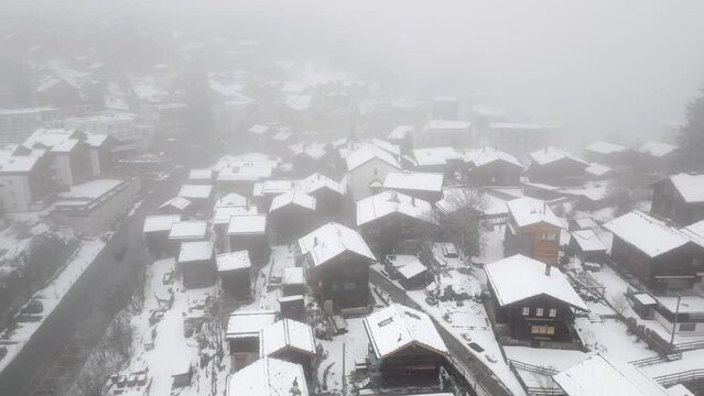 Snowy mountain village Blatten Belalp in fog and snow with small chalets, huts and alpine huts. Aerial Shot