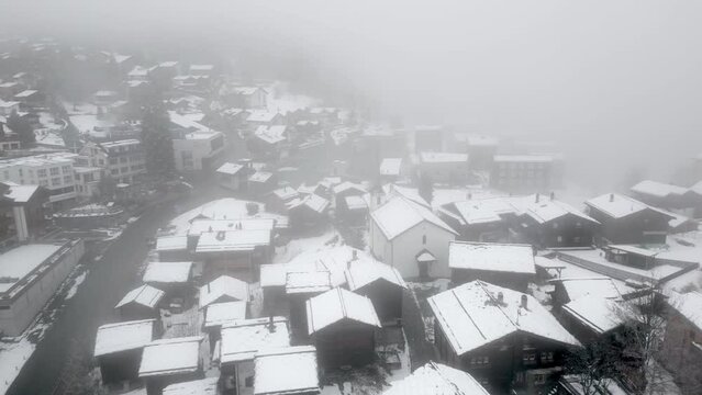 Snowy mountain village Blatten Belalp in mist and snow with small chalets, cabins and alpine cottages. Aerial Shot