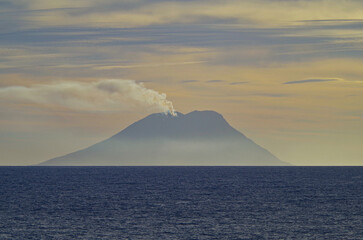 Fototapeta na wymiar Stromboli volcano at horizon with clouds of smoke coming from summit seen from outdoor deck of luxury cruiseship cruise ship liner during Mediterranean cruising at twilight