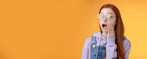 Shocked impressed speechless young redhead sensitive european girl glasses wearing hoodie dungarees...