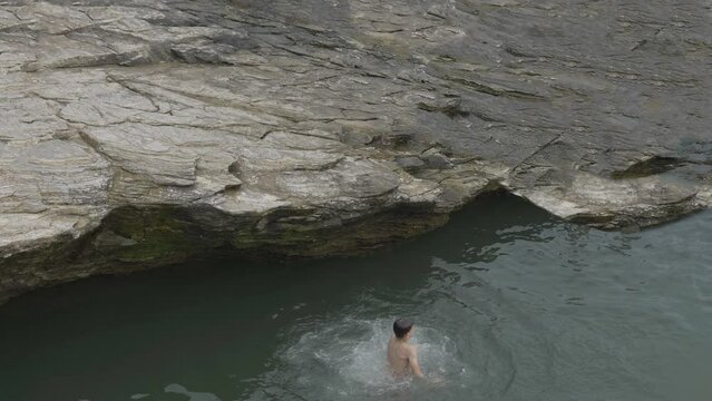 Kid jumping from the cliff into the lagoon, enjoy summer vacation at seaside