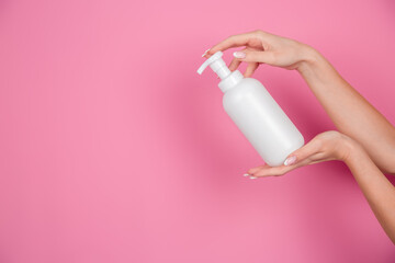 female hands on a pink background hold a bottle of shampoo or shower gel