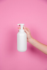 female hands on a pink background hold a bottle of shampoo or shower gel