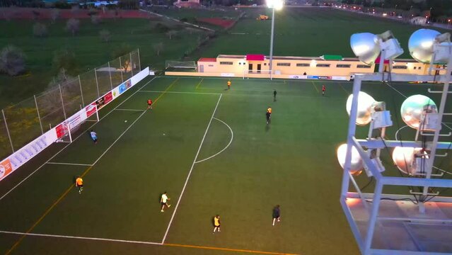 Slow drone shot of people playing football rotating behind a light post of a field at Santa Ponsa, Mallorca, Spain.