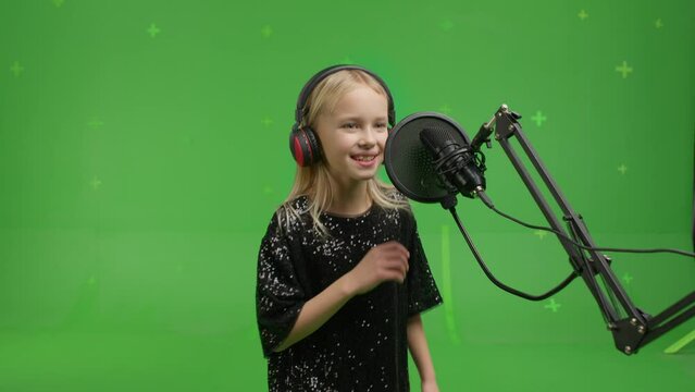 close-up of portrait of young girl singing into a studio microphone on a green screen background.