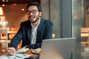 Smiling businessman working with graphs and charts at modern cafe and looking at side