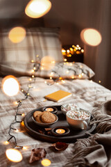 warm cozy bedroom interior with cup of hot chocolate on tray, candles christmas lights