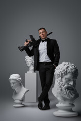 Shot of secret agent dressed in classic suit holding rifle around sculptures.