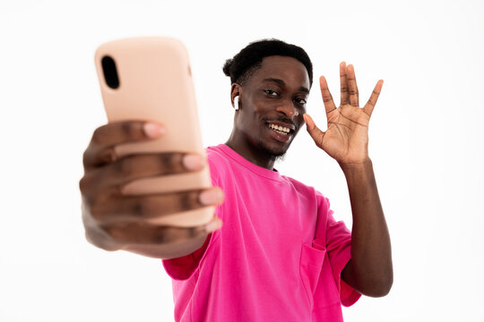 Smiled african american fashionable man waving at camera talking by video link with girlfriend wearing erphones and holding new smartphone standing posing for camera.