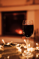A glass of red wine on a glass table near the fireplace. Christmas Eve
