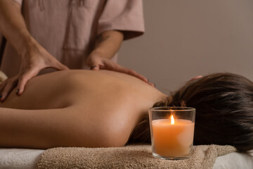 Fototapeta na wymiar Female masseur does a relaxing back massage in a spa salon with lit candles. Concept of health, body care