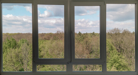 A large panoramic window with a beautiful view of the forest in spring. Springtime landscape with tree tops.