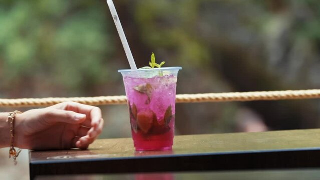 Female hand puts a refreshing drink  to table ,on the bank of mountain river.  blur nature background. close up, 4k.
