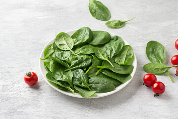 Plate with fresh spinach leaves and cherry tomatoes on a light gray background. delicious healthy...
