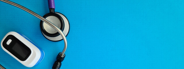 Modern fingertip pulse oximeter and stethoscope on blue background