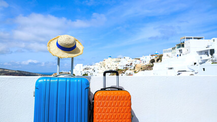 Summer concept with two luggage with hat and landscape view of Oia town in Santorini island in Greece , Greek landscape as blue sky background - obrazy, fototapety, plakaty