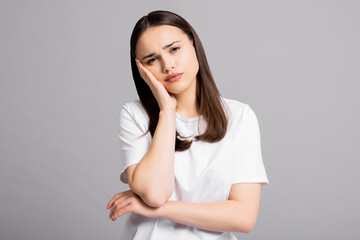 Obraz premium Sad exhausted young girl woman with headache suffering from migraine standing on grey background in studio isolated closing eyes holding arm near head.
