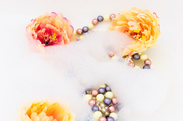 Fototapeta na wymiar Multicolored beads and peonies in foam. copy space. top view