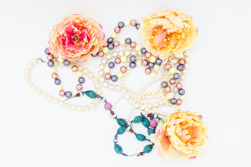 Multi-colored beads and pearl necklace among peony flowers. copy space. top view