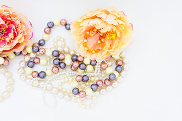 Multi-colored beads and pearl necklace among peony flowers. top view. copy space