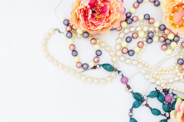 Multi-colored beads and pearl necklace among peony flowers. copy space