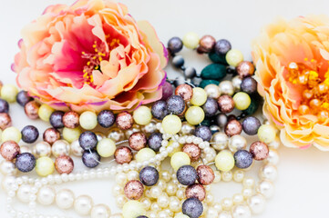 Multi-colored beads and a necklace of pearls on a pink peony background. Selective focus. Close up