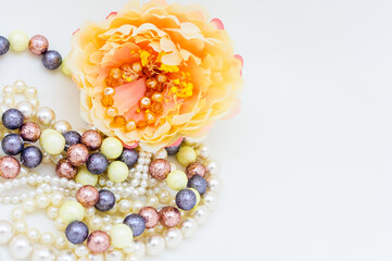 Multicolored beads and a pearl necklace next to a yellow flower. copy space