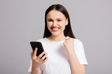 Portrait of young attractive adorable lovely pretty cute successful cheerful woman winning celebrating isolated on grey background holding cellphone showing delighted emotions at camera.