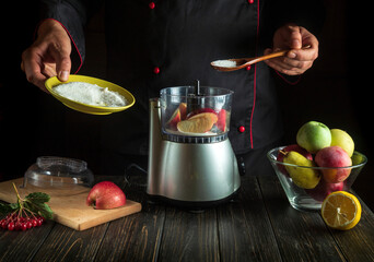 Professional chef prepares fresh apple juice in an electric blender. The cook adds sugar to the...