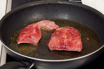 Top sirloin marbled American beef steak kitchen cooking. High-angle focus of raw meat on a hot pan with olive oil.
