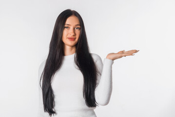 Pleased young brunette woman holding palm open for new product or sale presentation. Happy girl look at the camera, stand over white studio background, copy space for promotion