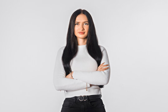 Portrait of serious lady posing with folded arms over white studio background. Confident young woman in closed posture. Office professions