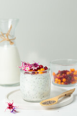 Dessert with yogurt, chia seeds, wild berries and edible flowers. Close-up on a light background. A glass of berries and a jug of milk in the background