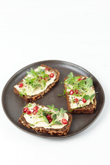 Healthy toasts on black bread with soft goat cheese, sprouts, microgreens and pomegranate seeds. On a white background