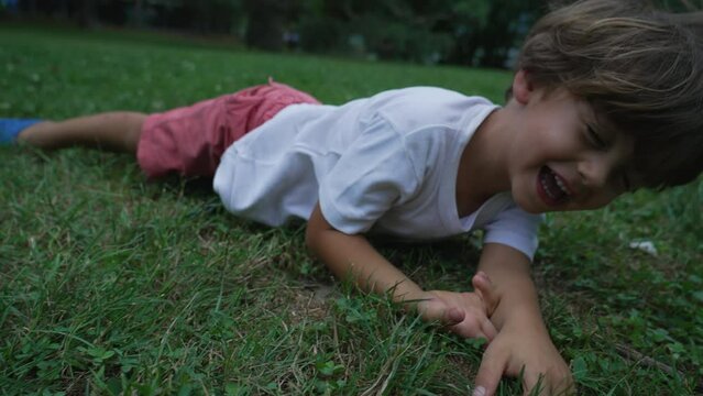 One happy child laid on grass outside smiling and laughing. Close up face of male kid lying at park