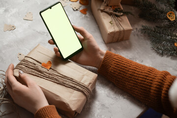 Fototapeta premium a young woman holds a phone, a tablet in her hand and fulfills an order by phone, taking an order for gift wrapping, in the background a Christmas tree and lights