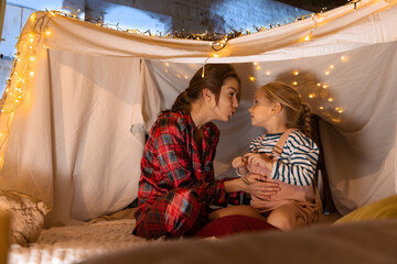 Obraz na płótnie Canvas Happy family. Mother and daughter in pajamas sitting inside self-made hut, tent in room in the evening. Cozy time