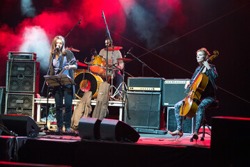 Rock group playing on the live concert outdoor in summer. Guitar player, singer, drummer and cellist.