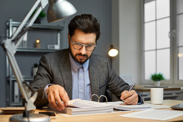 Serious business man, auditor, bookkeeper or financial accountant in a suit and glasses sitting at...