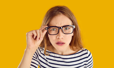 Hey, what did you say. Dissatisfied young woman has focused look and stares at you intently through glasses. Girl who feels disappointed after hearing something unpleasant. Orange background.
