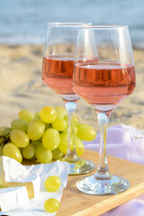 Glasses with rose wine and snacks for beach picnic on sandy seashore, closeup