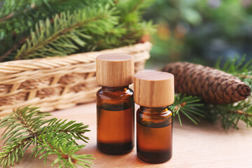 Bottles of pine essential oil, cone and branches on wooden table, closeup