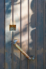 An old wooden handle and an internal lock on a dark wooden door with shadows